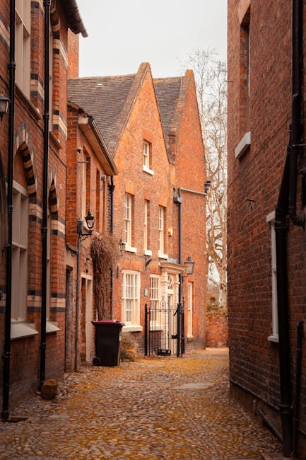 A narrow residential street in Connaught Village featuring closely spaced brick terraced houses with small front gardens enclosed by low brick walls and sloped tiled roofs. The street surface is aspha