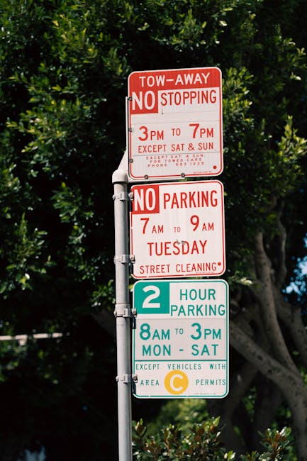A white rectangular parking sign attached to a wooden post outside a building featuring large windows with reflective glass panes. The sign displays a blue handicap accessibility symbol, indicating a 